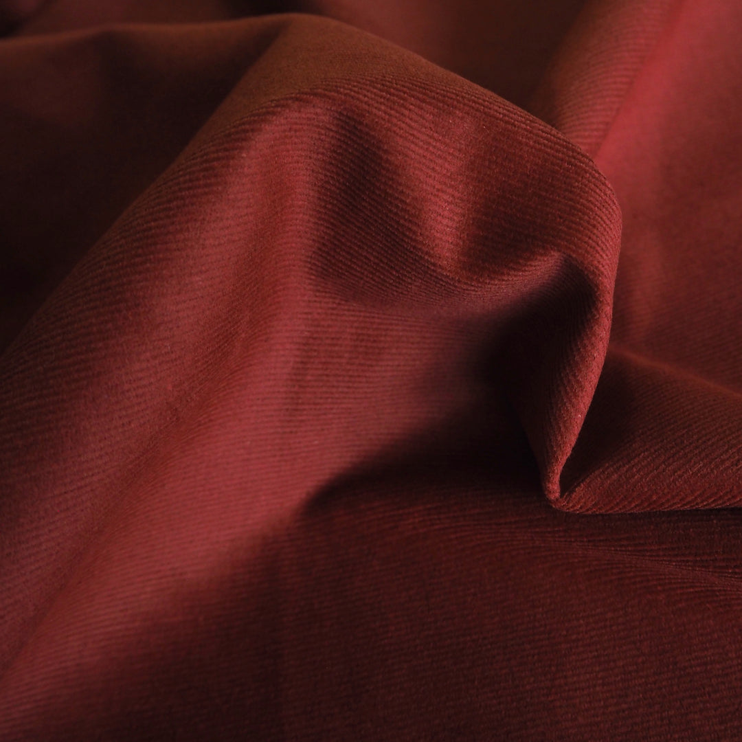 Dark amber stretch cotton needlecord fabric, fine cord texture.