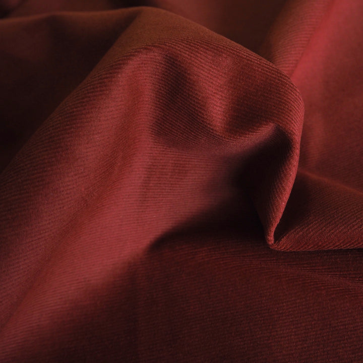 Dark amber stretch cotton needlecord fabric, fine cord texture.