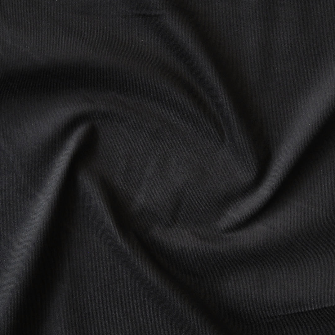 Black stretch cotton needlecord fabric, soft fine cord texture.