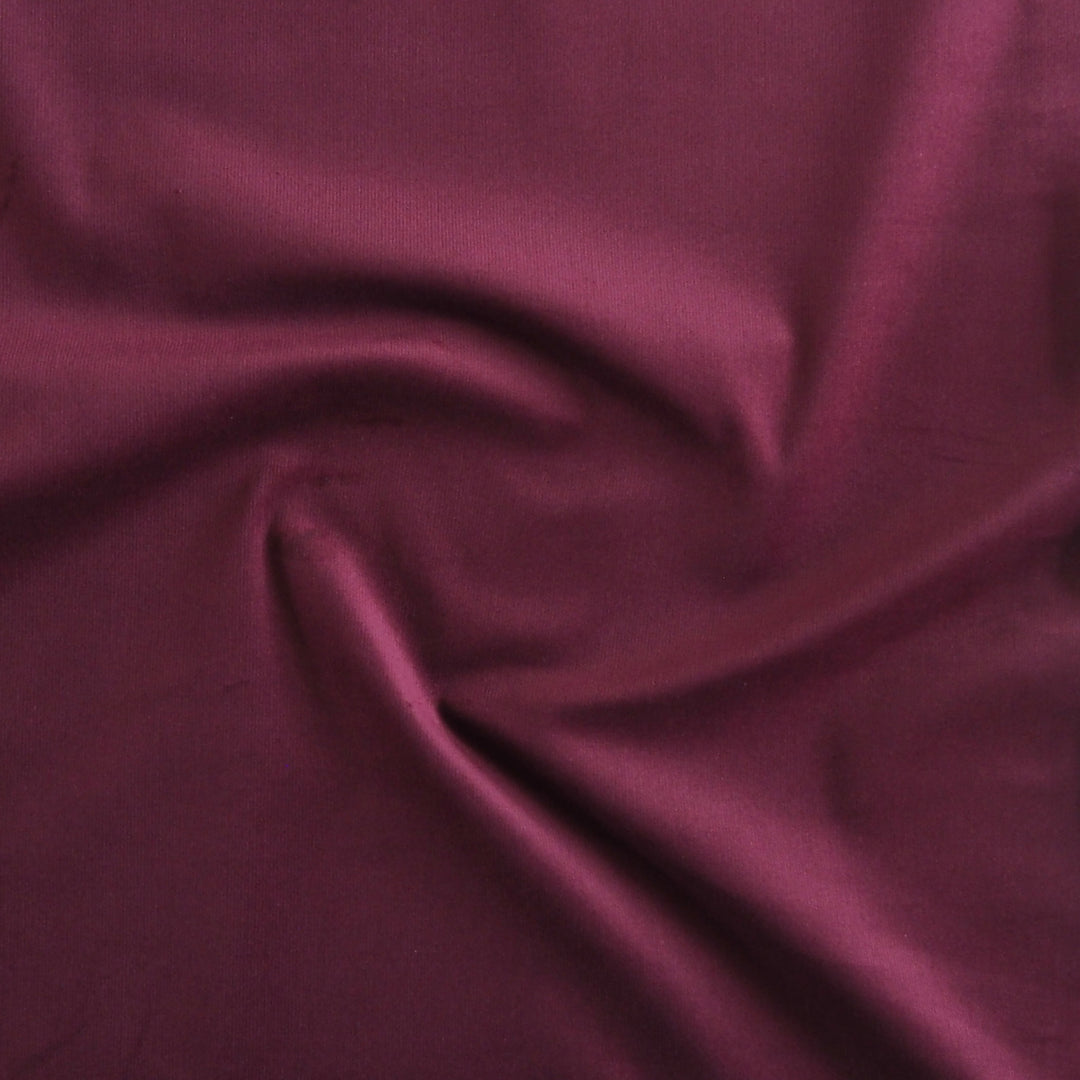 Cranberry red stretch cotton needlecord fabric, fine cord texture.