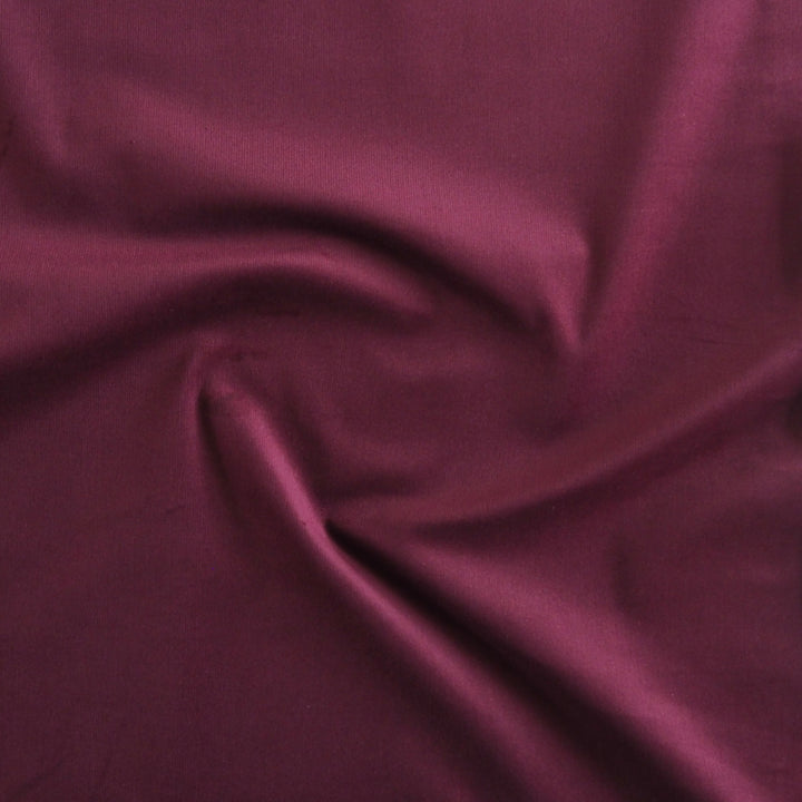 Cranberry red stretch cotton needlecord fabric, fine cord texture.