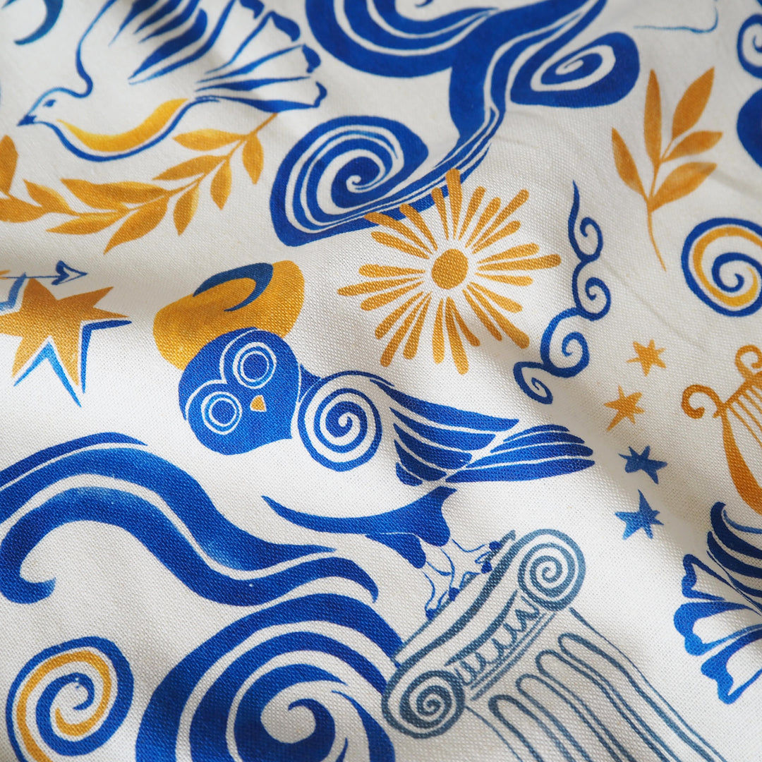 Close-up of fabric with blue and orange patterns including birds, suns, and swirls.