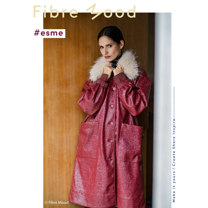 Woman wearing a red coat with fur collar against a wooden background, Fibre Mood brand visible.