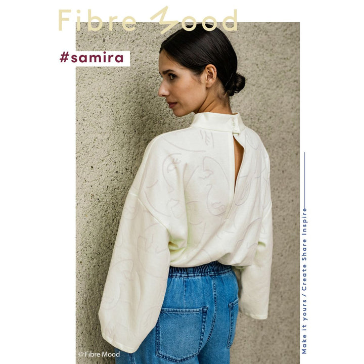 Woman wearing a white open-back shirt and blue jeans against a textured wall with 'Fibre Mood' branding.