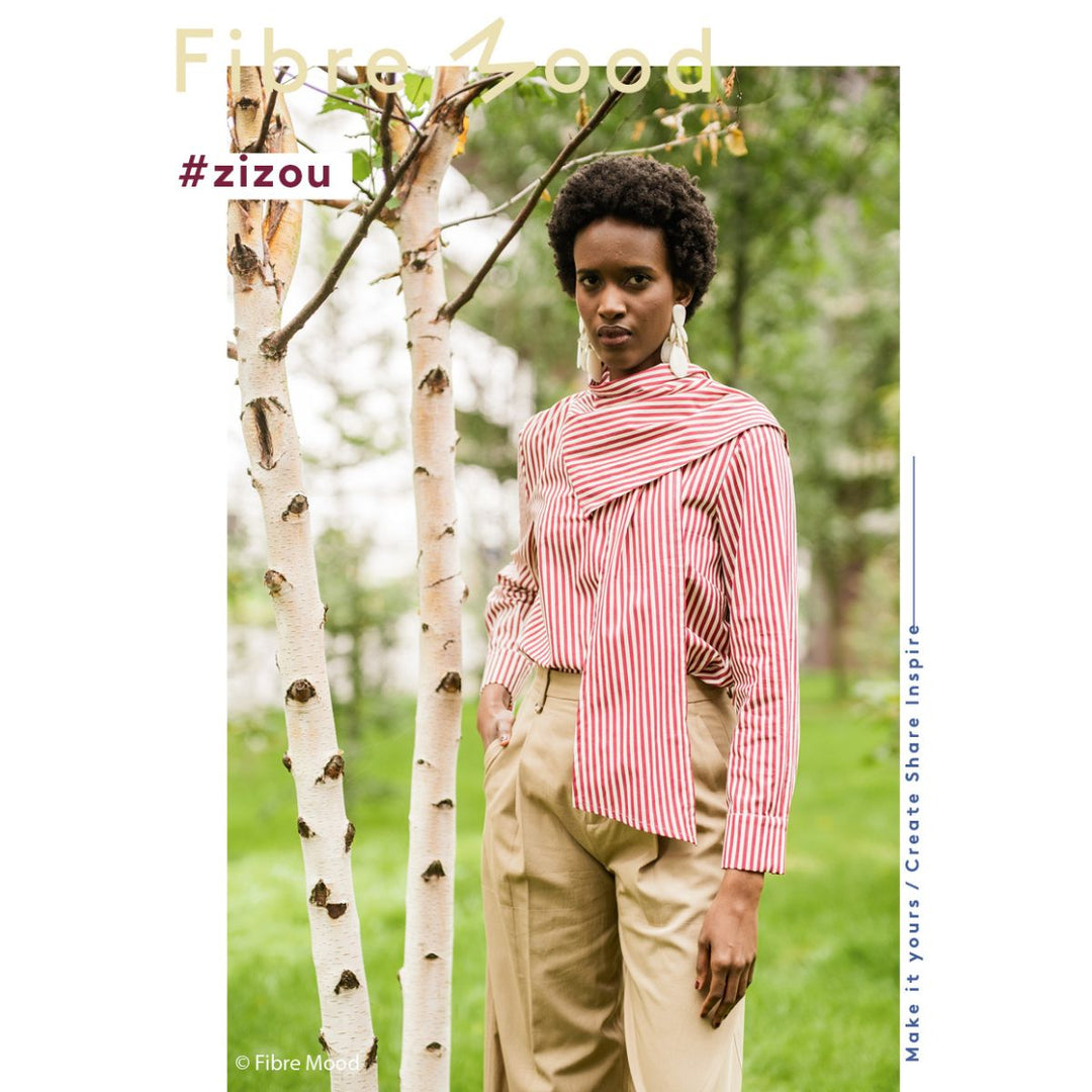 Woman wearing a red and white striped shirt and beige pants standing in a natural setting with trees.