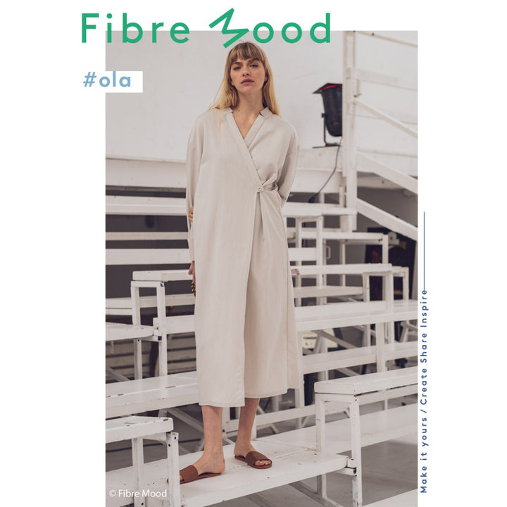 Woman wearing a light-colored dress standing on white stairs with 'Fibre Mood' branding.