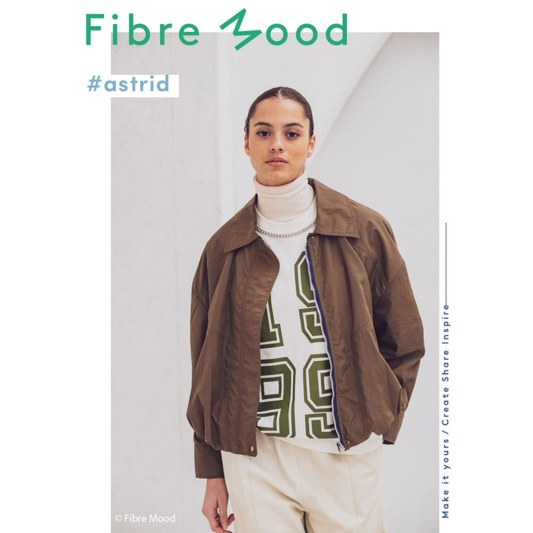 Person wearing a brown jacket over a white turtleneck with a graphic design, standing against a plain background with 'Fibre Mood' branding.