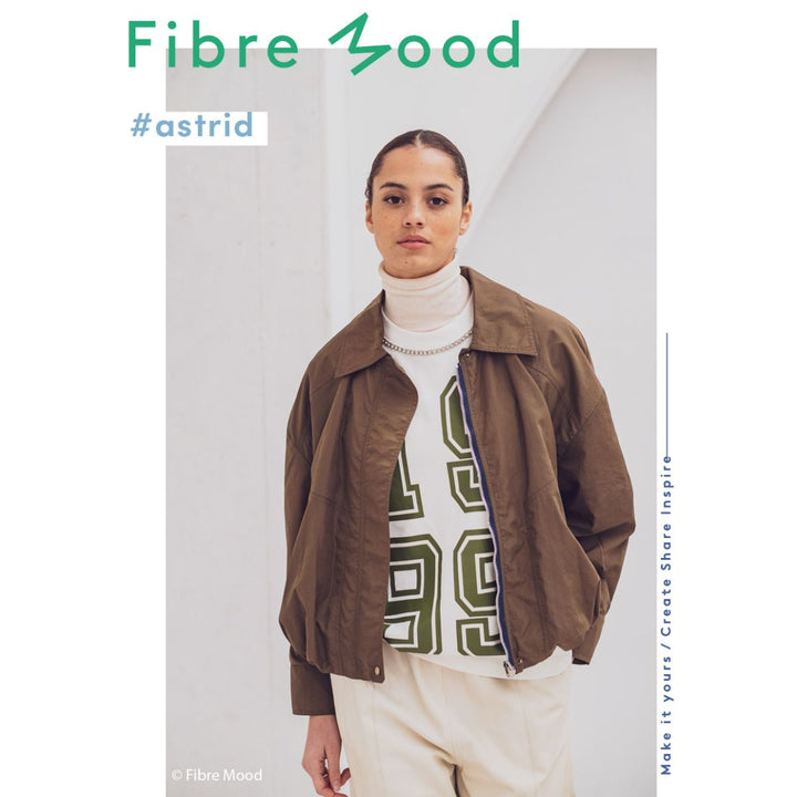 Person wearing a brown jacket over a white turtleneck with a graphic design, standing against a plain background with 'Fibre Mood' branding.