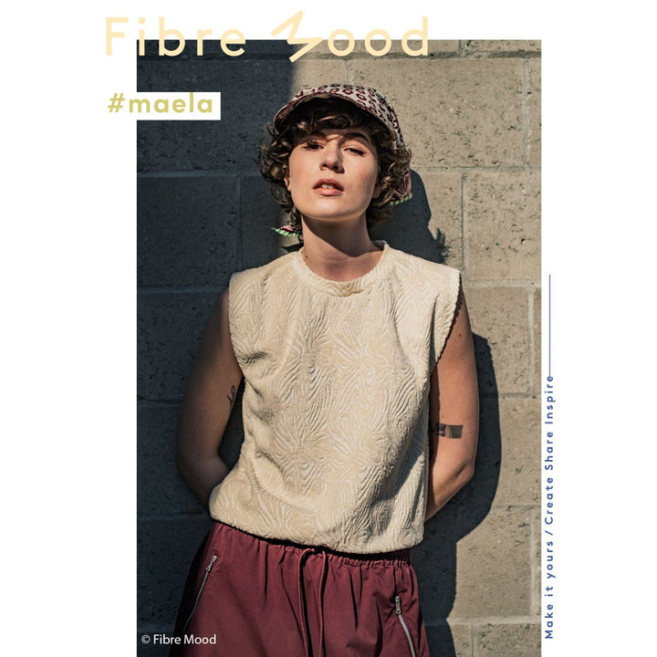 Person wearing a beige sleeveless top and maroon pants against a stone wall with 'Fibre Mood' branding.