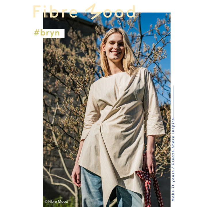 Woman wearing a beige top and blue jeans standing outdoors with 'Fibre Mood' branding.