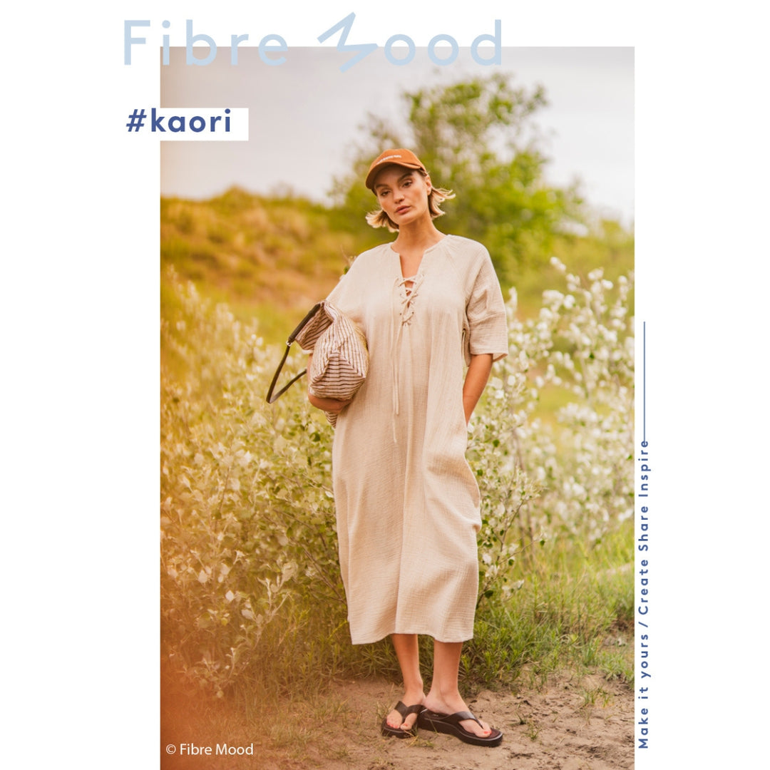 Woman in a beige dress standing in a field with 'Fibre Mood' branding.