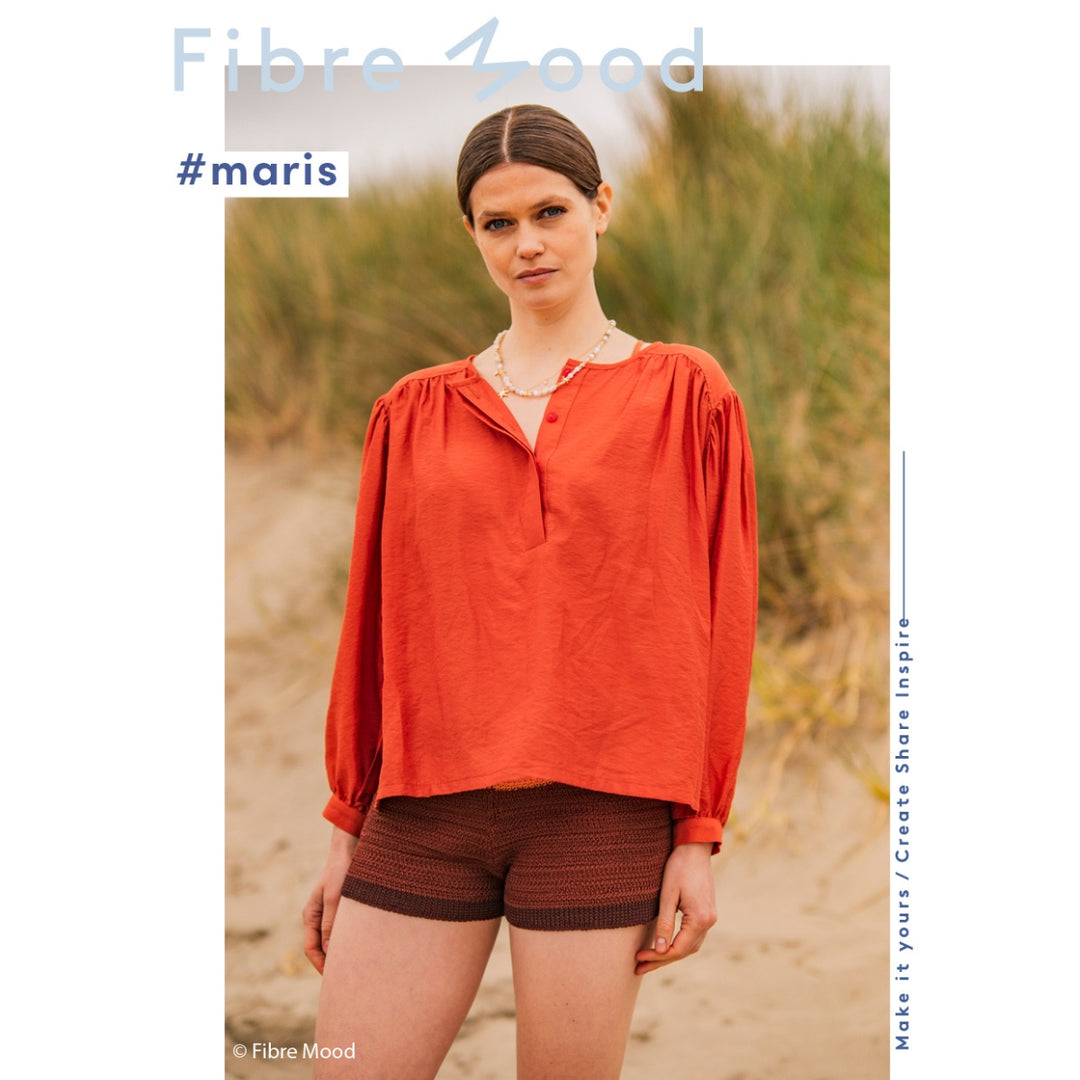 Woman wearing an orange blouse and brown shorts standing on a beach with 'Fibre Mood' branding.