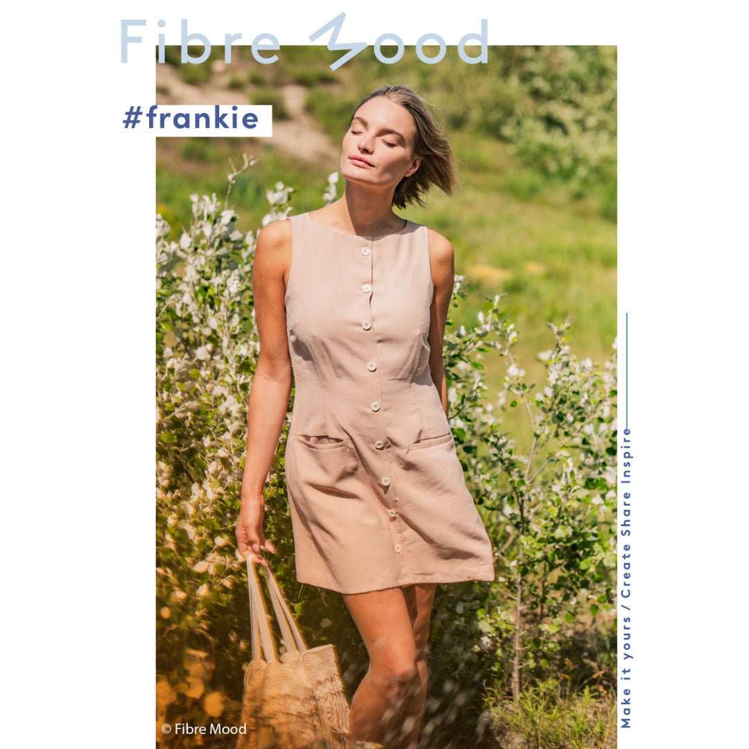 Woman in a beige dress standing in a field with 'Fibre Mood' branding.