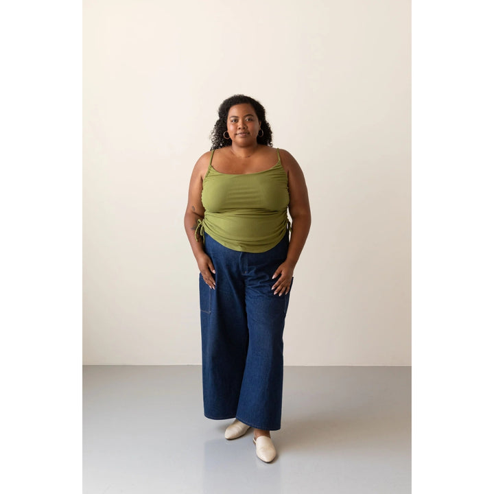 A woman modeling a sage green ribbed tank top and wide-leg blue jeans against a plain off-white studio background.