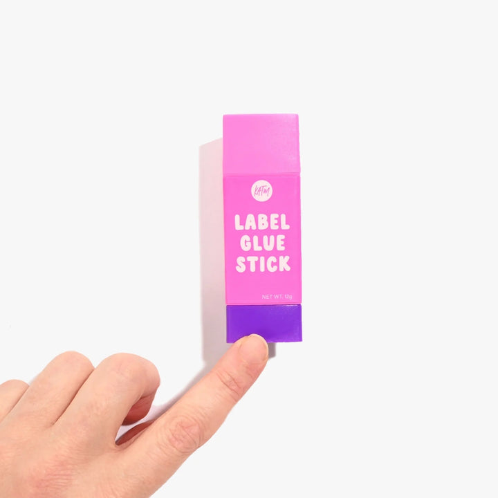 Hand holding a pink and purple label glue stick box on a white background
