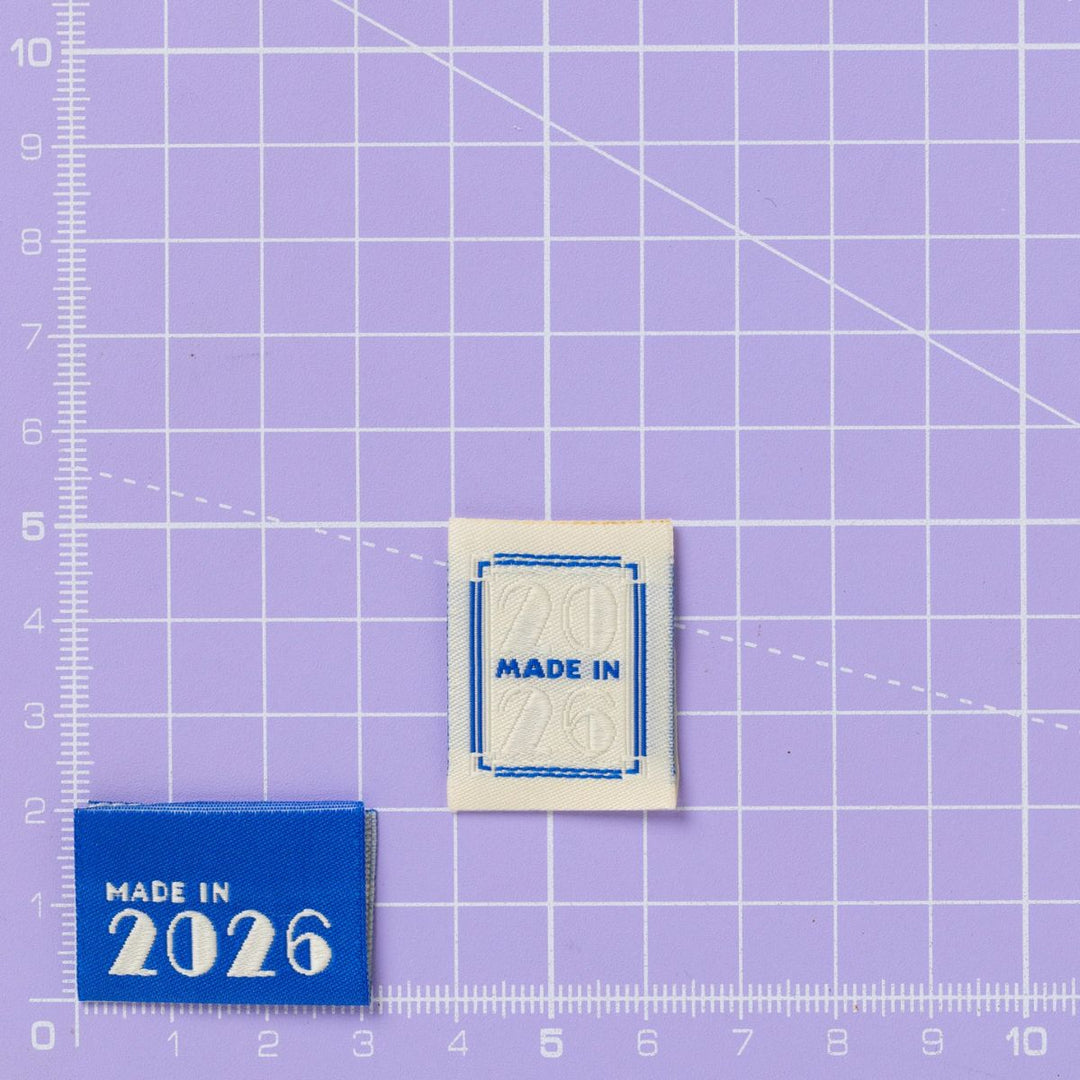 Two fabric patches labeled 'MADE IN 2026' on a purple grid background