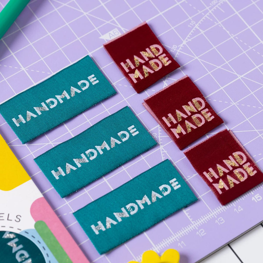 Colorful 'HANDMADE' labels on a purple cutting mat with a ruler.