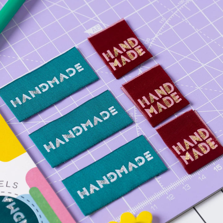 Colorful 'HANDMADE' labels on a purple cutting mat with a ruler.