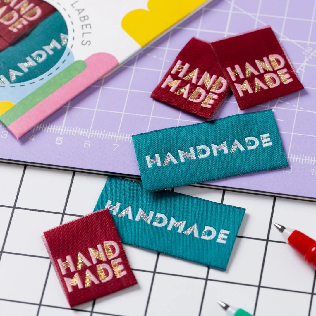 Handmade labels in red and teal on a cutting mat with grid lines.