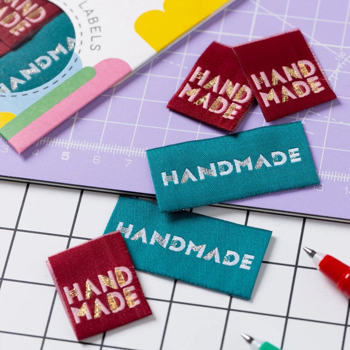 Handmade labels in red and teal on a cutting mat with grid lines.