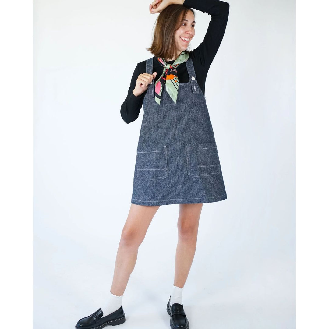 Woman wearing a denim pinafore dress with a colorful scarf against a white background