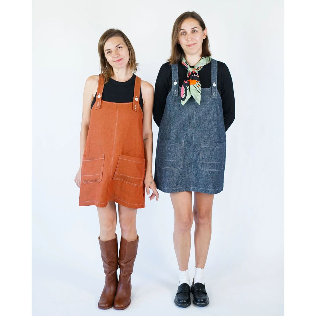 Two women wearing orange and blue denim pinafore dresses on a white background
