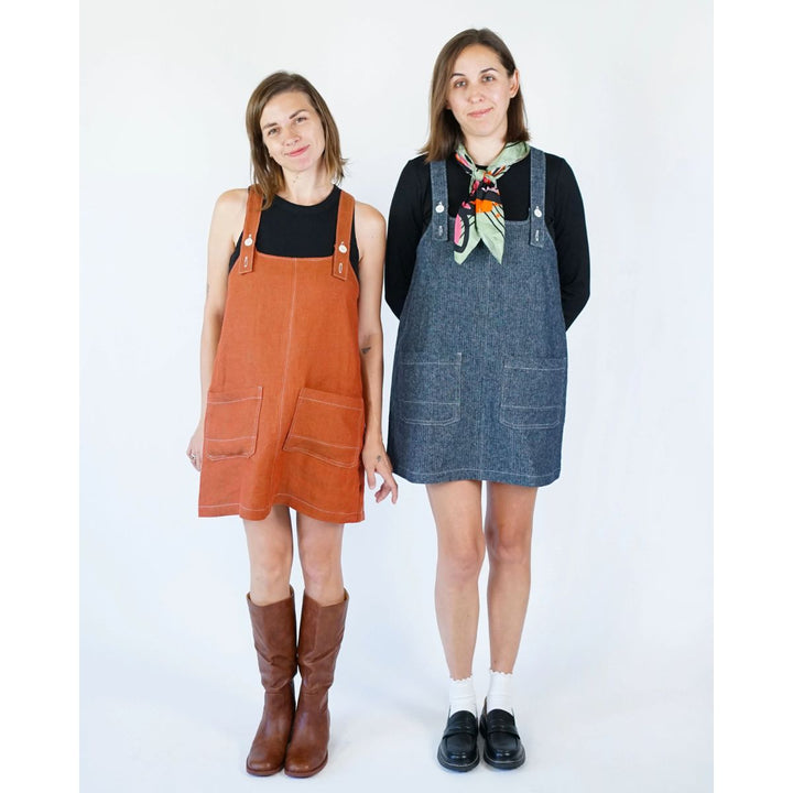 Two women wearing orange and blue denim pinafore dresses on a white background