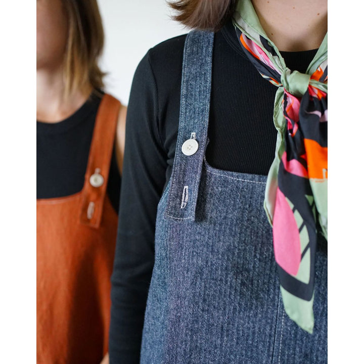Person wearing a denim overalls with a colorful scarf around their neck.