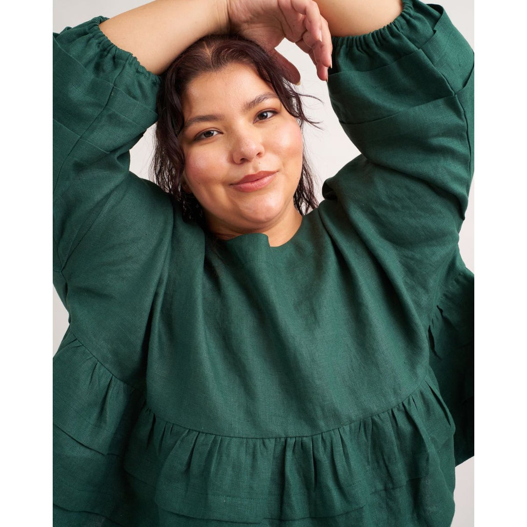 Woman wearing a green dress with her hands above her head against a plain background