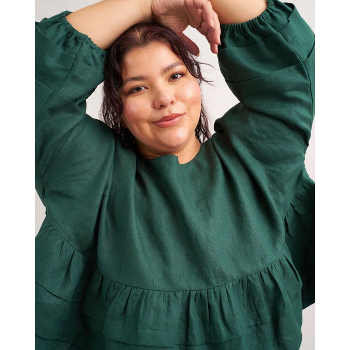 Woman wearing a green dress with her hands above her head against a plain background
