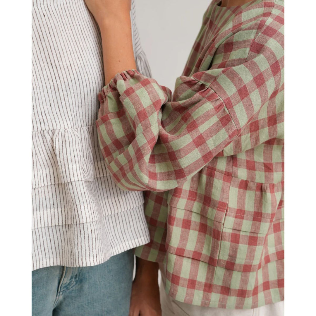Person wearing a red and green checkered shirt with a white and gray striped shirt in the background.