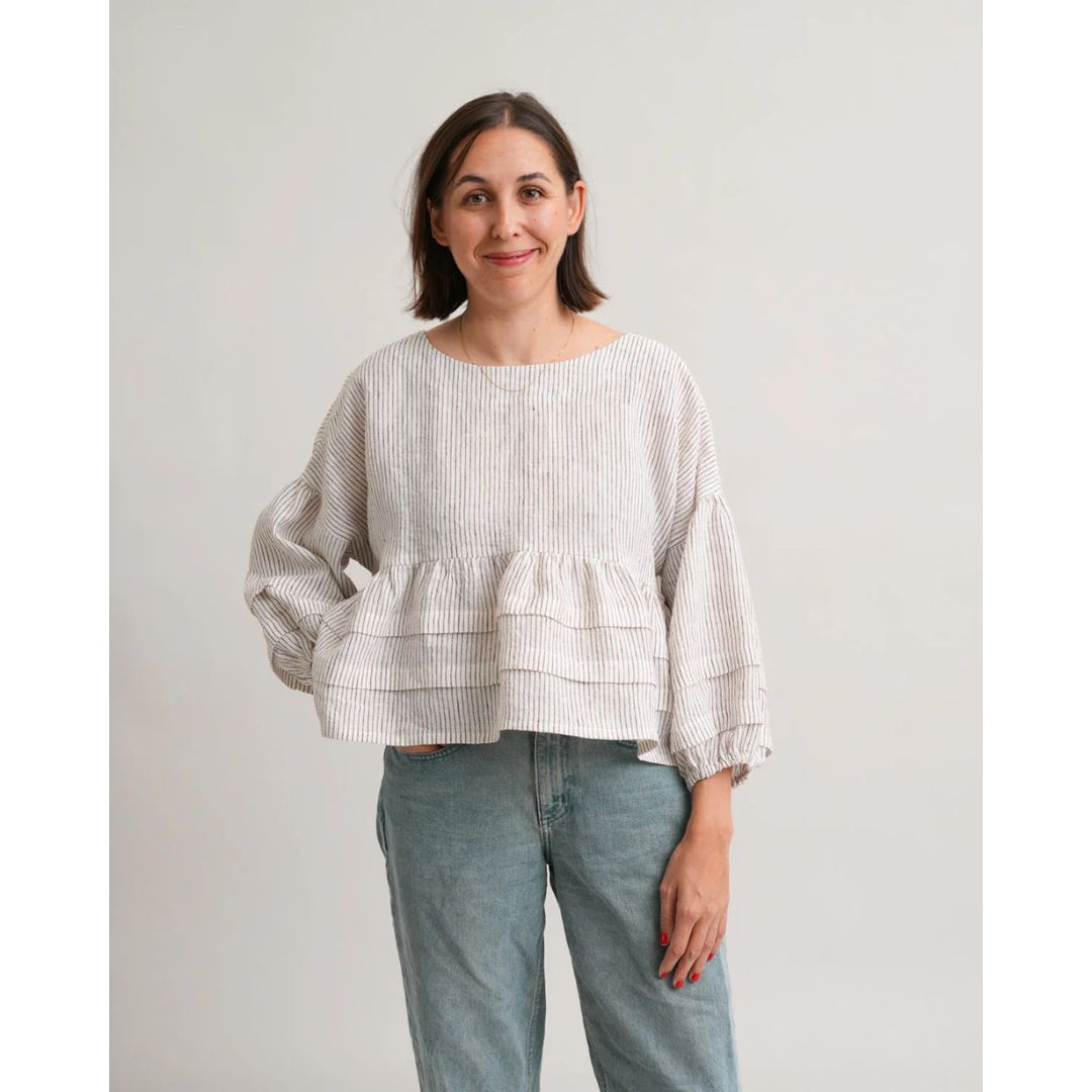 Woman wearing a white ruffled blouse and blue jeans against a plain background