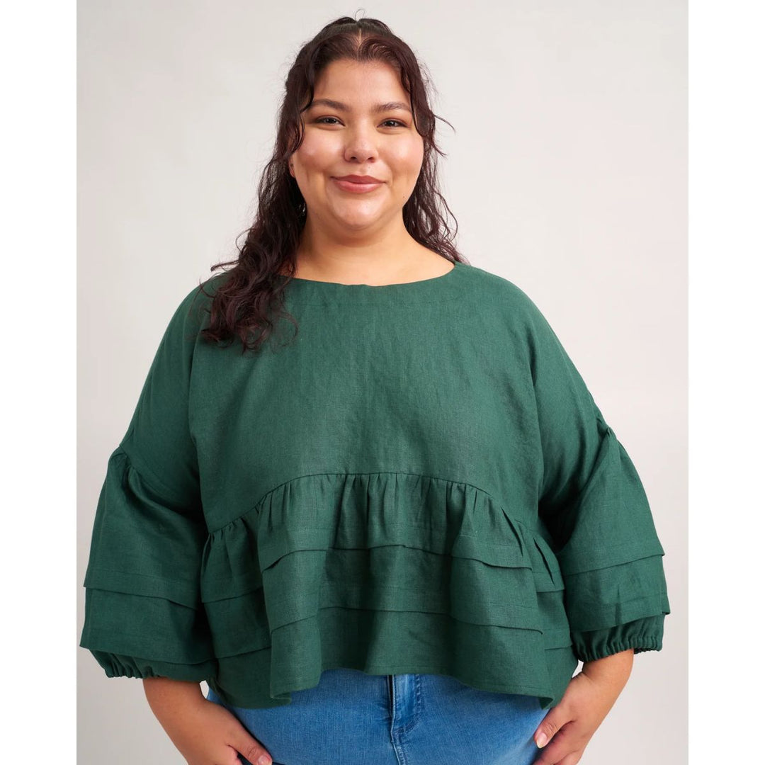 Woman wearing a green blouse with ruffled layers on a plain background