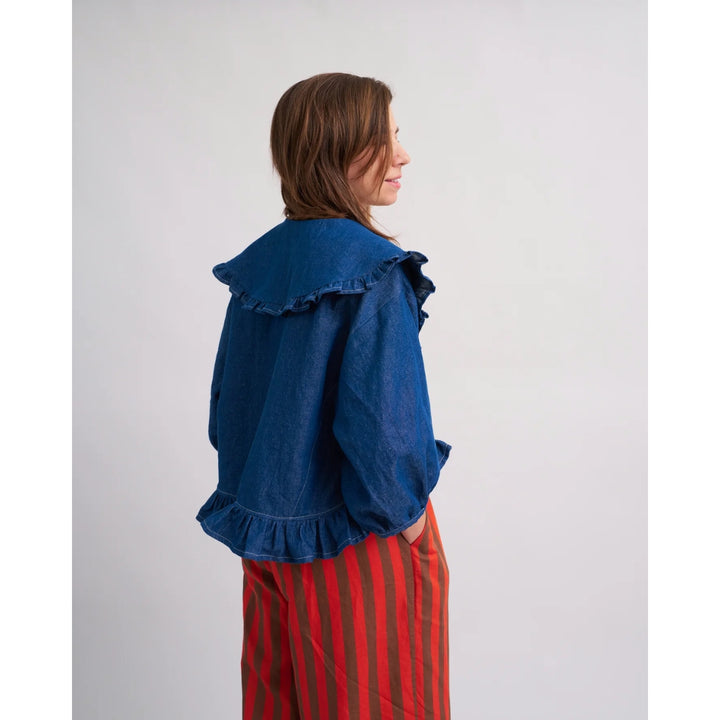 Woman wearing a blue denim jacket with ruffled details on a plain background