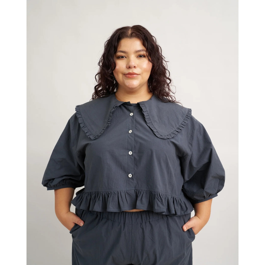 Woman wearing a dark blue outfit with ruffled details on a plain background
