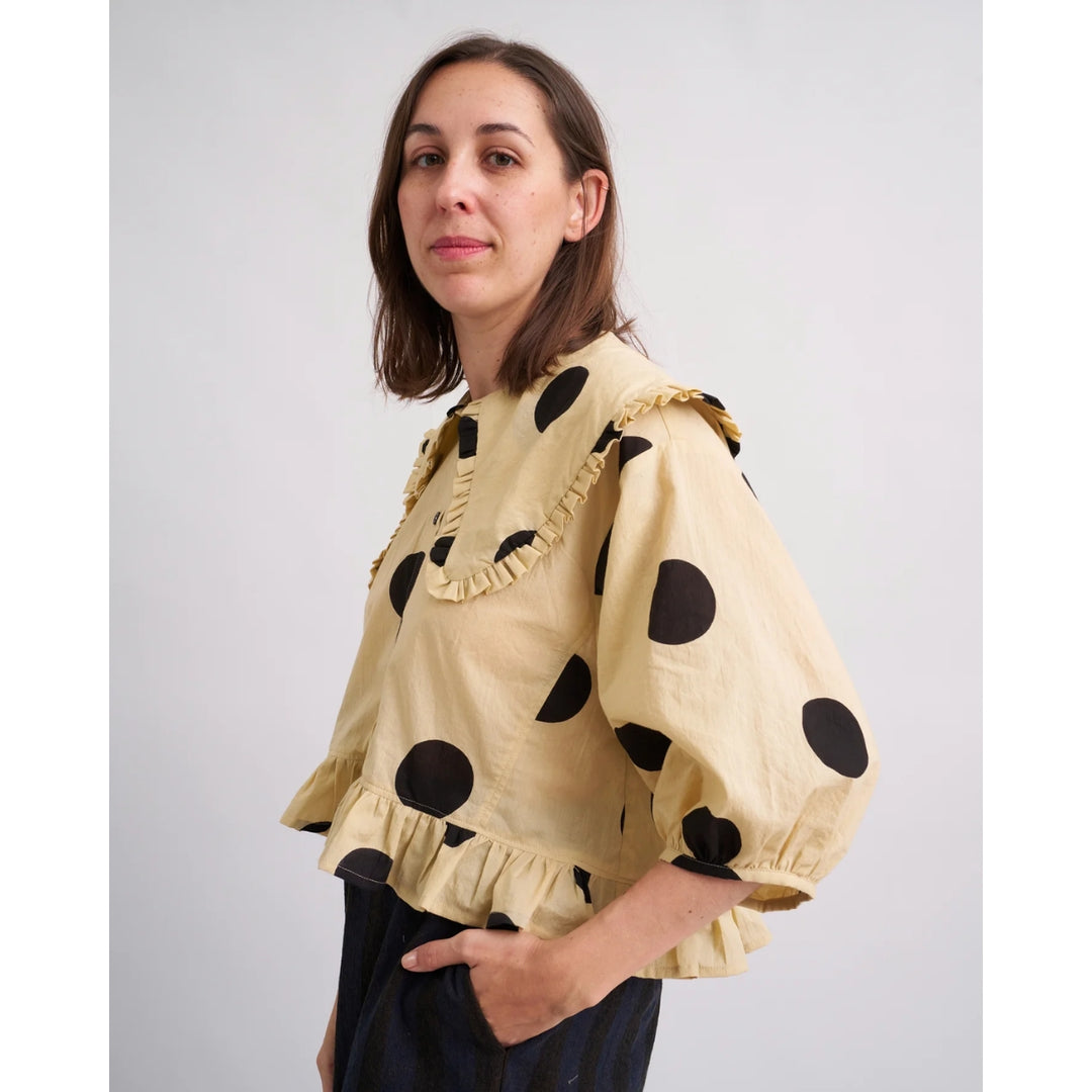 Woman wearing a beige blouse with black polka dots against a plain background