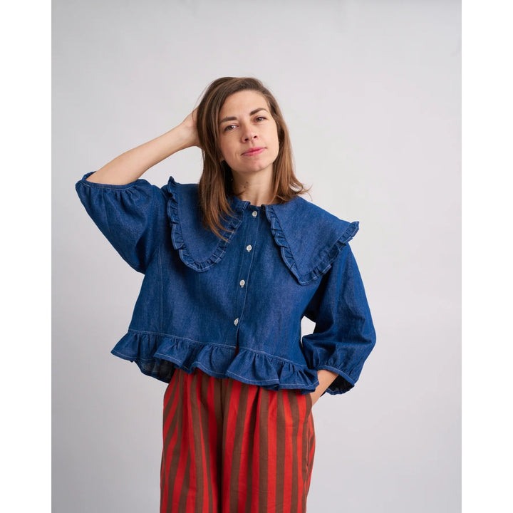 Woman wearing a blue denim blouse with ruffled details against a plain background