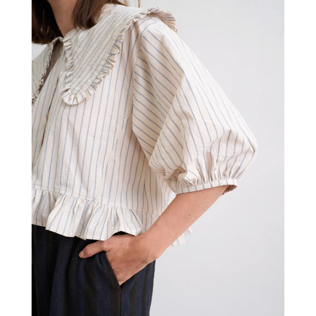 Woman wearing a white blouse with blue stripes and ruffled details on a plain background