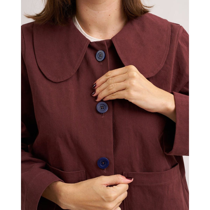 Close-up of a person wearing a burgundy coat with blue buttons on a white background