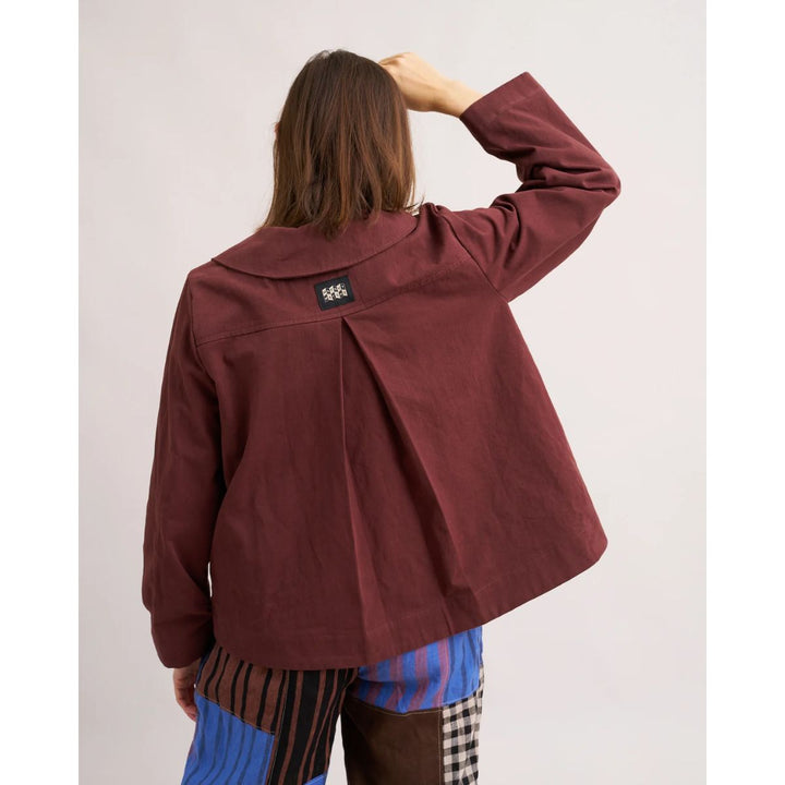 Person wearing a maroon jacket with a visible brand logo on the back, standing against a plain background.