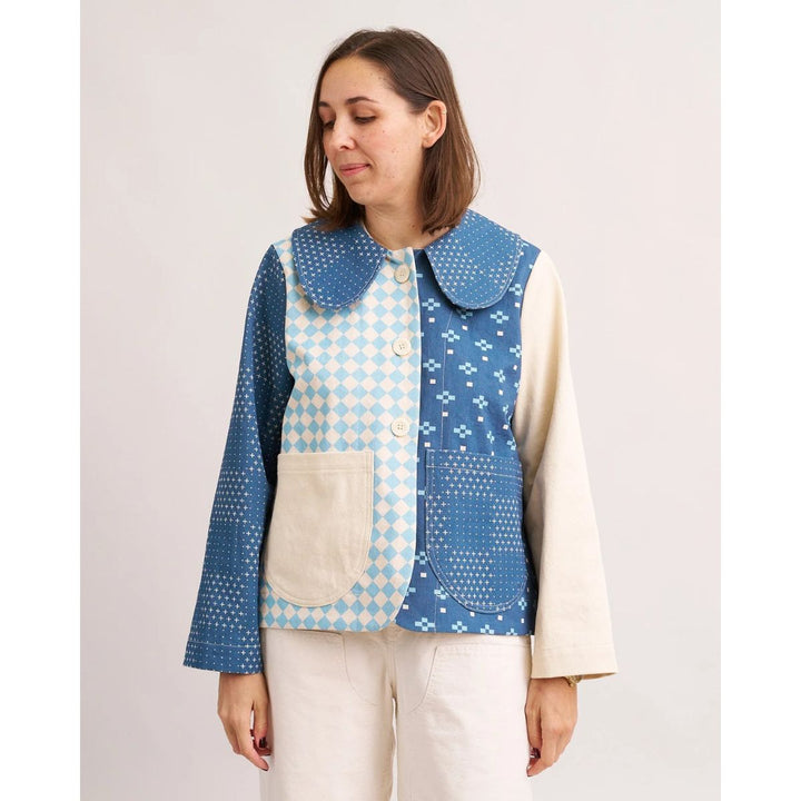 Woman wearing a blue and white patterned vest over a cream shirt on a plain background