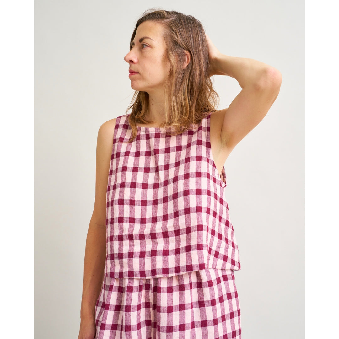 A woman wearing a sleeveless pink and white gingham check top and matching bottoms, standing against a plain light gray background.