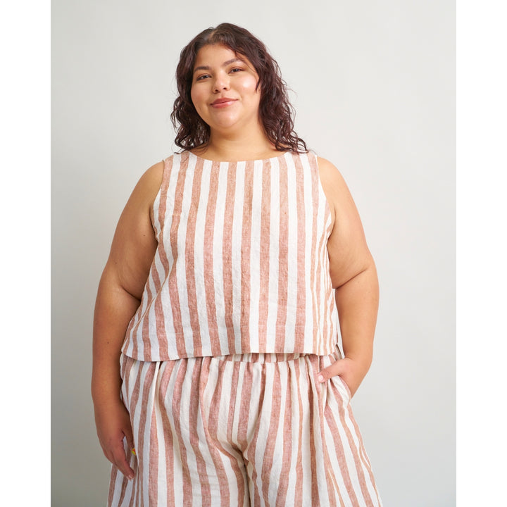 A woman modeling a sleeveless matching top and pants set with vertical pink and off-white stripes, photographed against a plain light gray studio background.