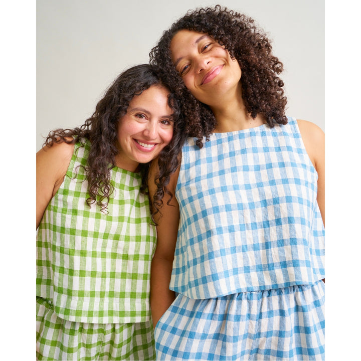 Two women posing together in matching gingham check outfits, one in green and white and the other in blue and white, against a plain light gray background.
