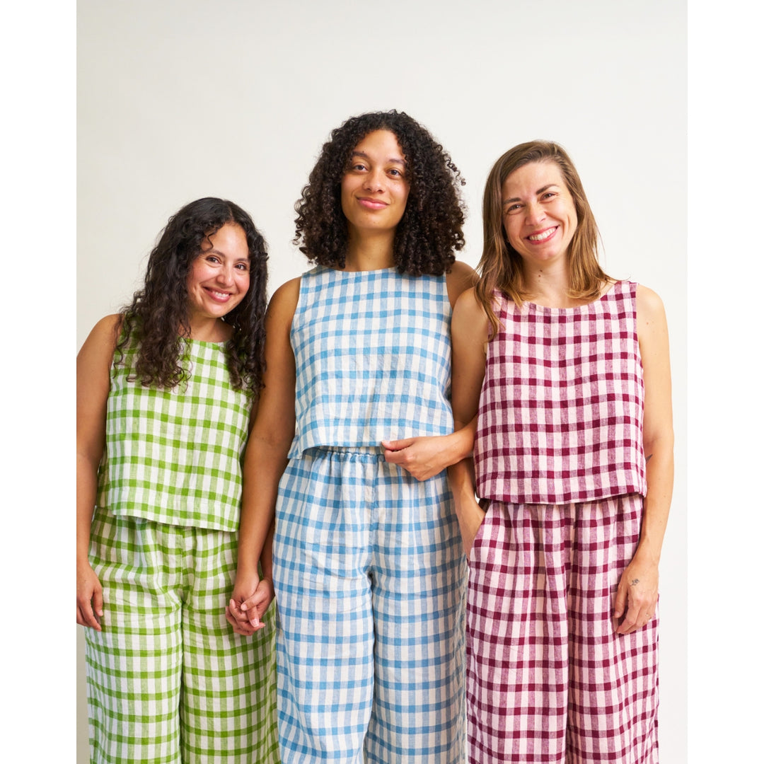 Three women standing side by side wearing matching sleeveless gingham outfits in green, blue, and red, against a plain light background.