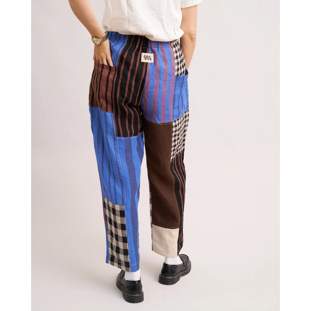 Person wearing a patchwork-style pants with blue, brown, and plaid patterns on a plain background.