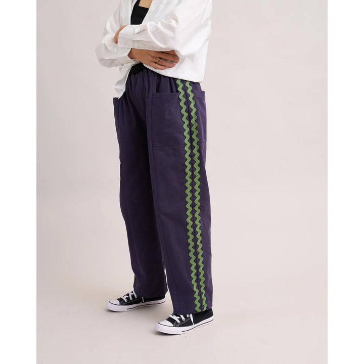 Navy pants with green zigzag stripes worn by a person on a light gray background