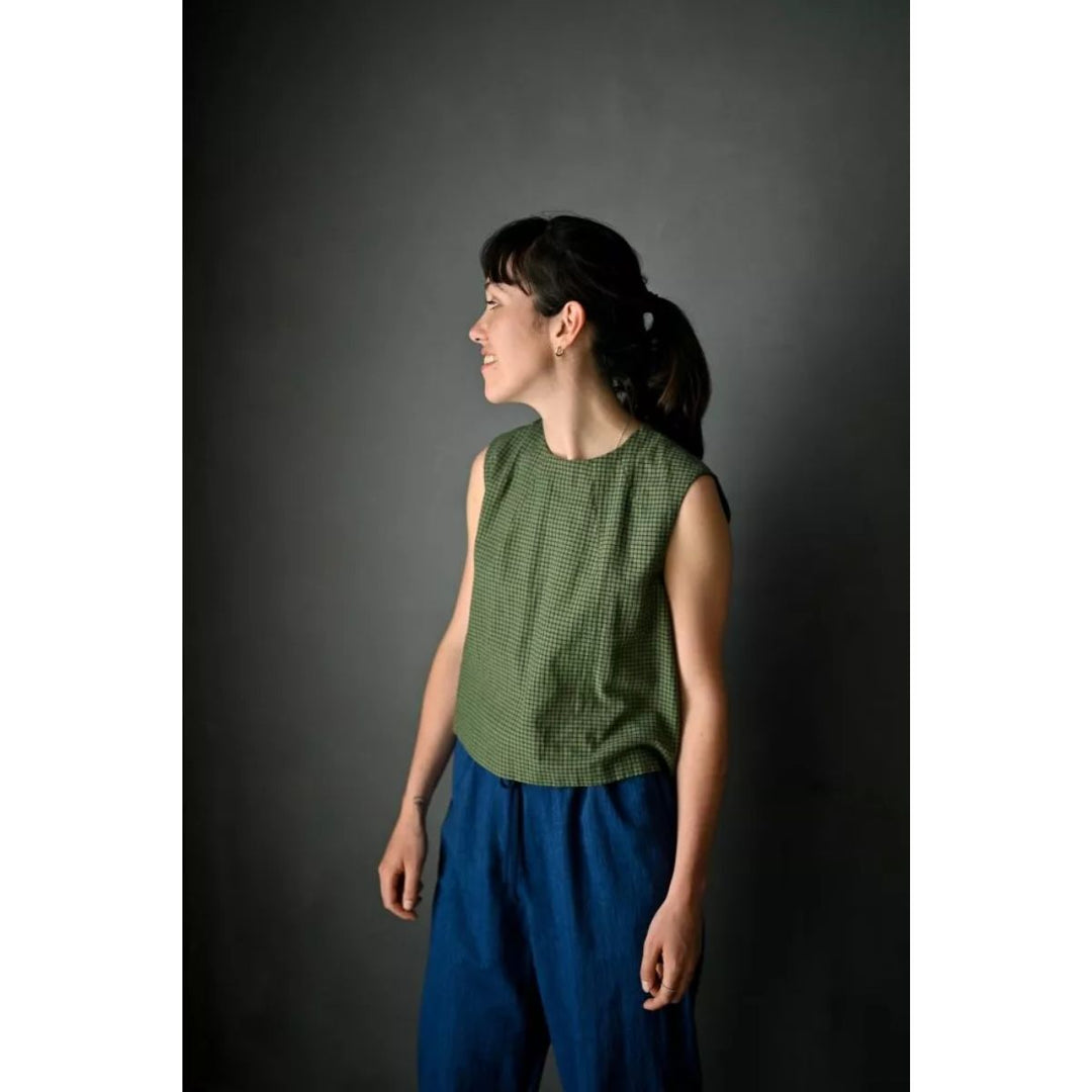 Woman wearing a green sleeveless top and blue pants against a dark background