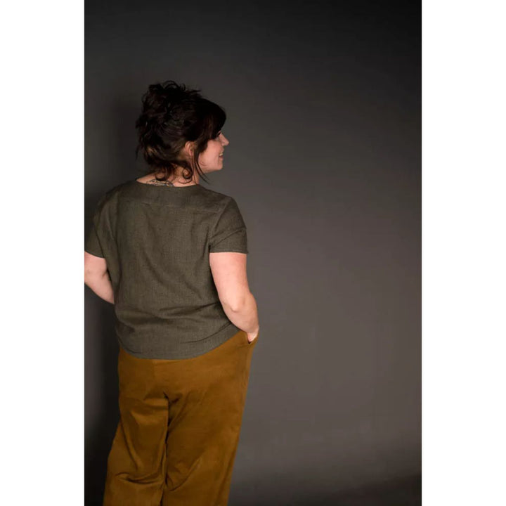 Person wearing a green shirt and brown pants against a dark background