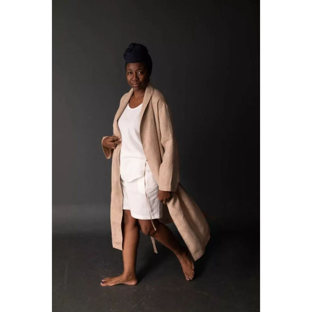 Person wearing a beige robe over a white outfit with a dark background